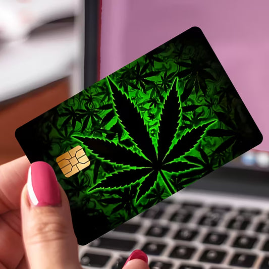 Card with cannabis leaf design held by a hand in front of a laptop.