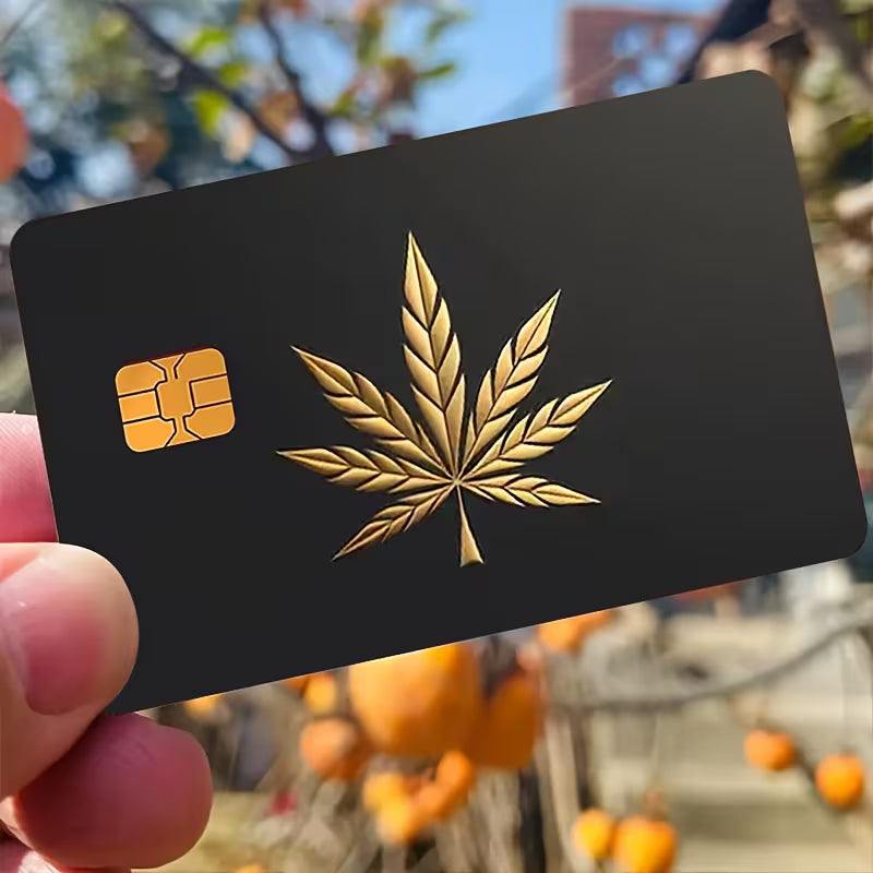 Black card with gold cannabis leaf held by a hand, blurred outdoor background